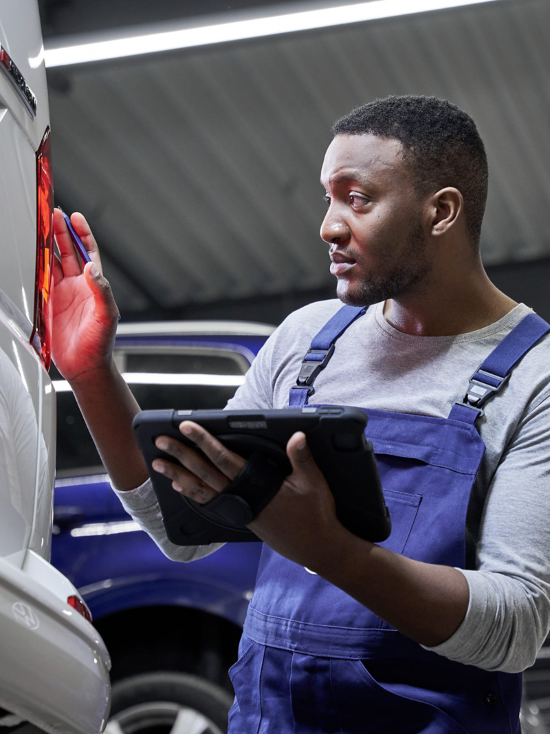 Die Rückscheinwerfer eines VW Multivan werden von einem Mechaniker mit Tablet geprüft.