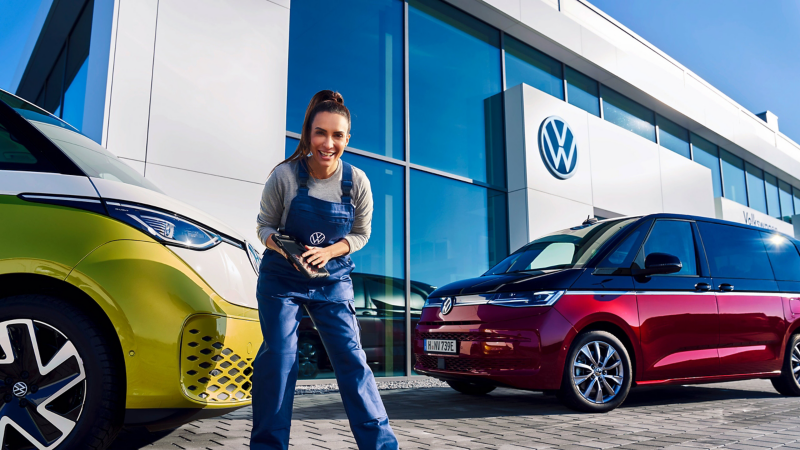 Eine Mechanikerin steht mit einem Tablet in der Hand vor einem Volkswagen ID. Buzz.