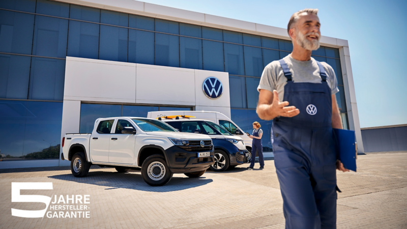 Ein VW Mitarbeiter vor einem Servicecenter mit vor dem Gebäude geparkten VW Fahrzeugen.