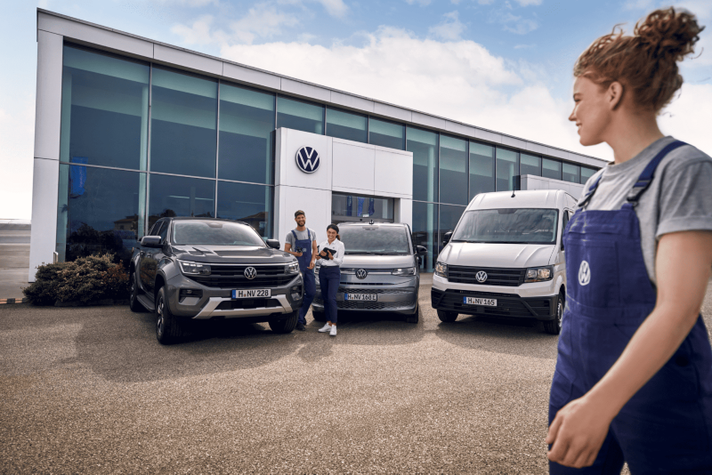 Pracownicy serwisu Volkswagena stoją przed salonem z trzema pojazdami marki Volkswagen.