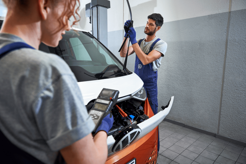 Wykwalifikowani mechanicy serwisują przednią szybę samochodu dostawczego marki Volkswagen.