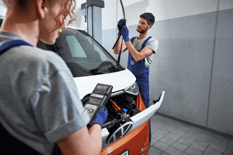 Wykwalifikowani mechanicy serwisują przednią szybę samochodu dostawczego marki Volkswagen.