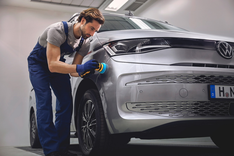 Pracownik serwisu poleruje zderzak dostawczego Volkswagena. 