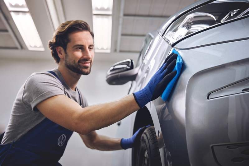 Pracownik serwisu czyści materiałową ścierką zderzak dostawczego Volkswagena.