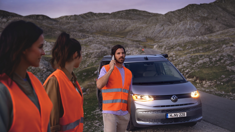 Drei Personen stehen vor einem Multivan und eine Person mit einem Handy am Ohr.