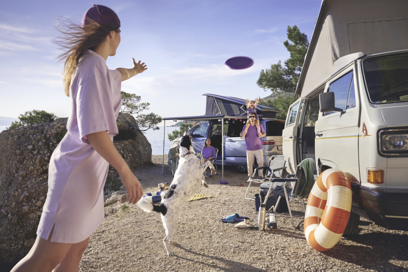 Deux personnes jouent au frisbee devant un California VW, dans un paysage d'été.