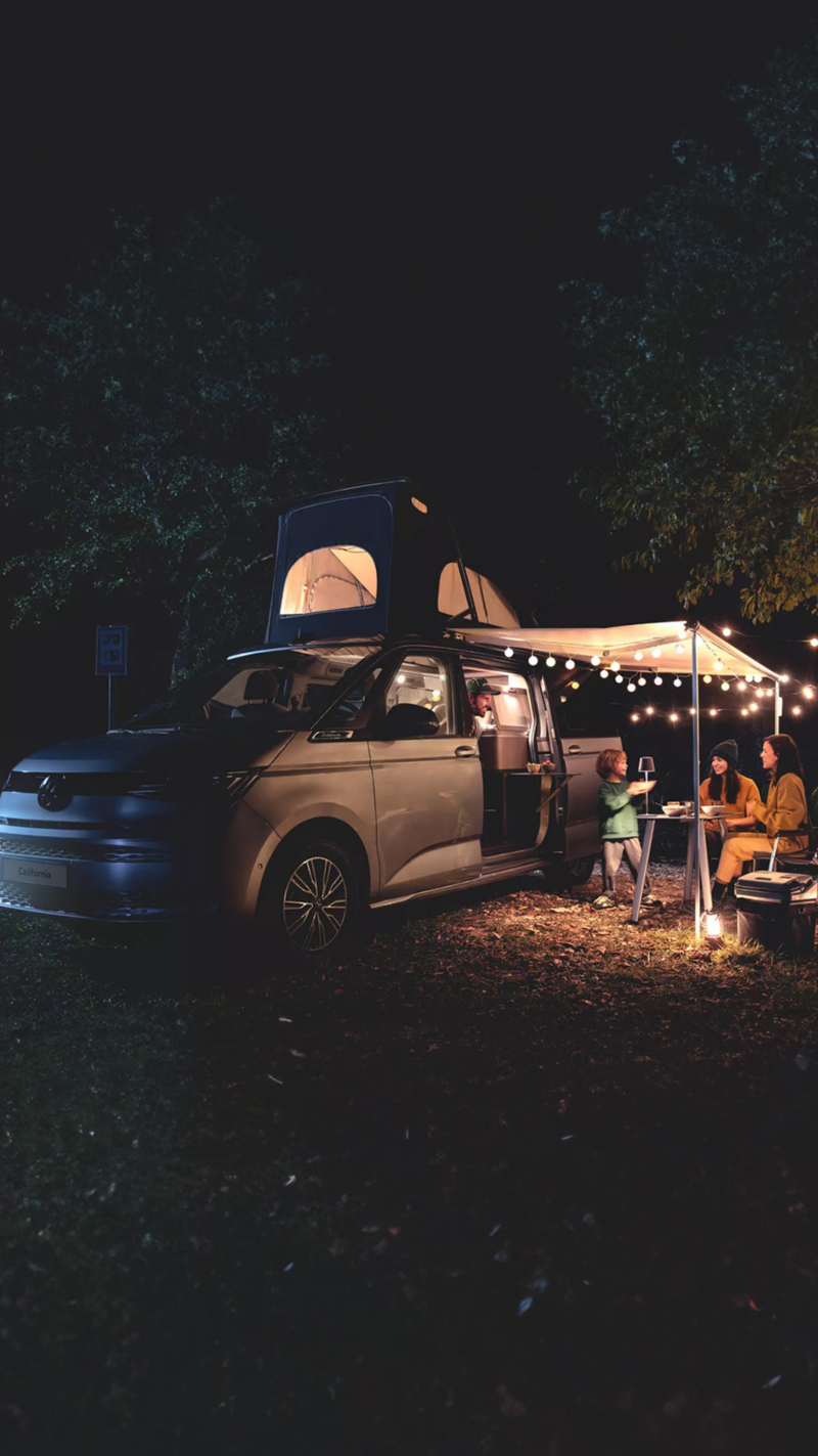 Photo showing a group of people eating food next to a VW California at night. 