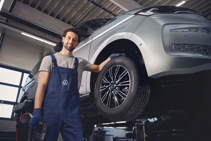 Pracownik serwisu stoi obok dostawczego Volkswagena na podnośniku.