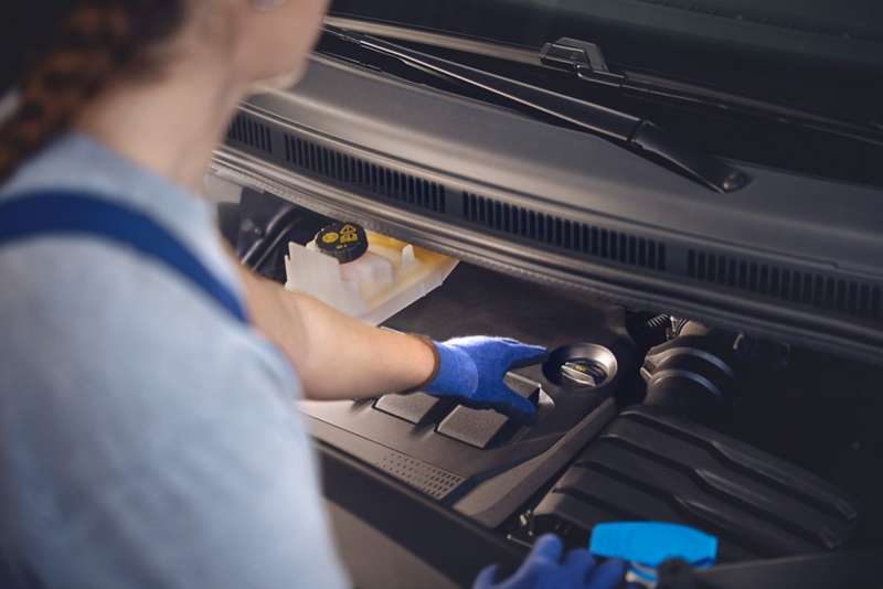 Pracownica serwisu sięga do korka od wlewu oleju silnikowego w dostawczym Volkswagenie.
