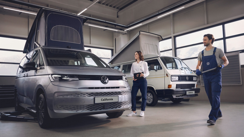 A photo showing two VW technicians inspecting some VW vehicles. 