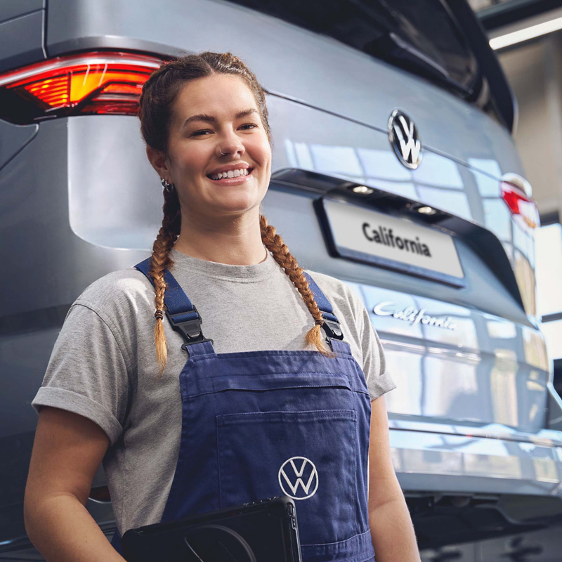 A smiling volkswagen technician standing in front of a California. 