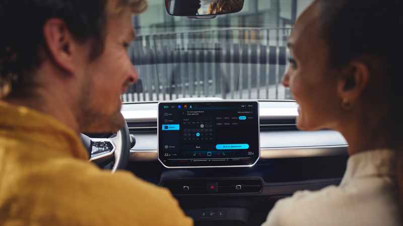Ein Mann und eine Frau benutzen das Infotainment-System im VW Auto und unterhalten sich.
