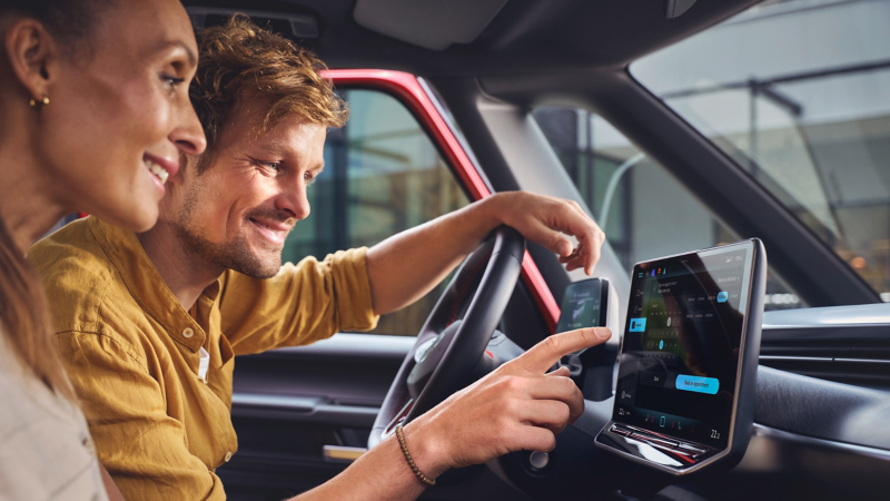 Eine Frau und ein Mann nutzen In-Car App Fahrzeugservice im VW Infotainment-System.