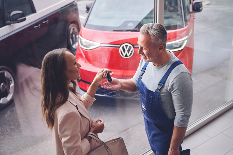 VW Servicemitarbeiterin überreicht Kundin Autoschlüssel, im Hintergrund ein ID. Buzz.