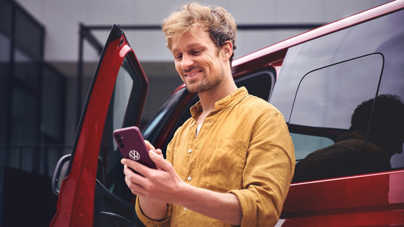 un homme devant son utilitaire VW regarde son smartphone utilisant les services VW Connect