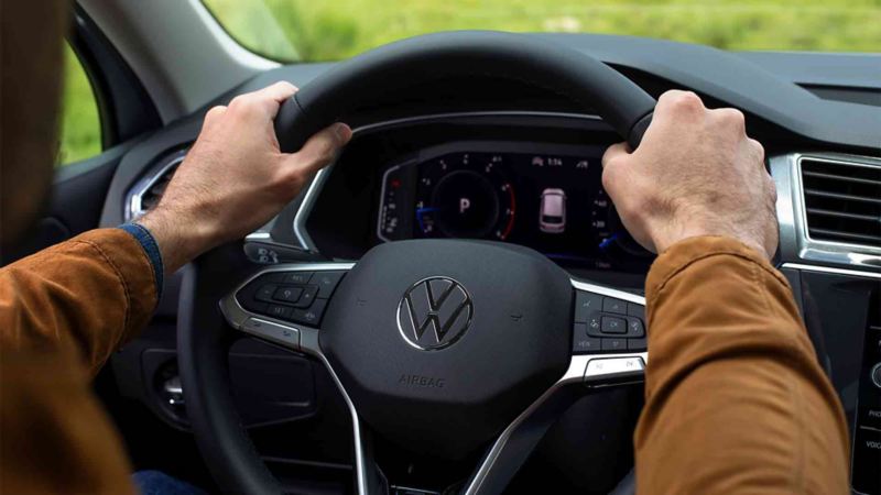 Mano de conductor manejando el volante de un auto Volkswagen en carretera.