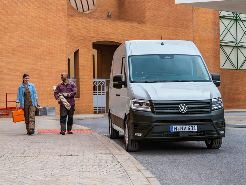 Un Crafter de ocasión aparcado en un exterior laboral y dos personas trabajadoras con materiales en sus manos