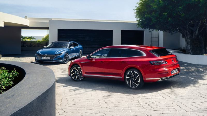 Ein roter Golf, ein weißer T-Cross und ein roter Tiguan stehen nebeneinander auf einem Parkdeck unter blauem Himmel.