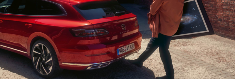 Man steekt zijn voet uit onder de achterbumper van een rode Arteon