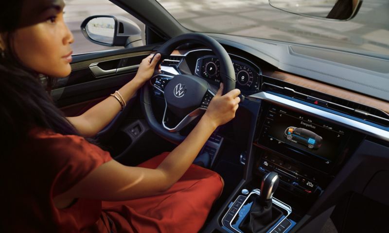 Женщина за рулем VW Arteon, смотрящая на рулевое колесо и сенсорный экран