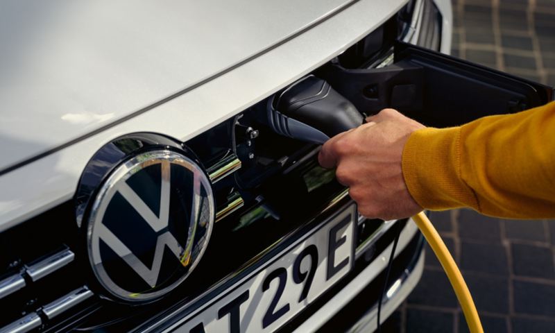 Nærbillede: Ladekablet sættes i stikdåsen i kølergrillen på en hvid VW Arteon Shooting Brake eHybrid.