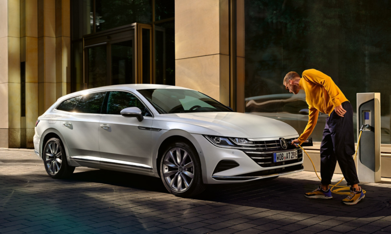 Hvid VW Arteon Shooting Brake eHybrid holder parkeret og oplader sættes i bilen af en mand