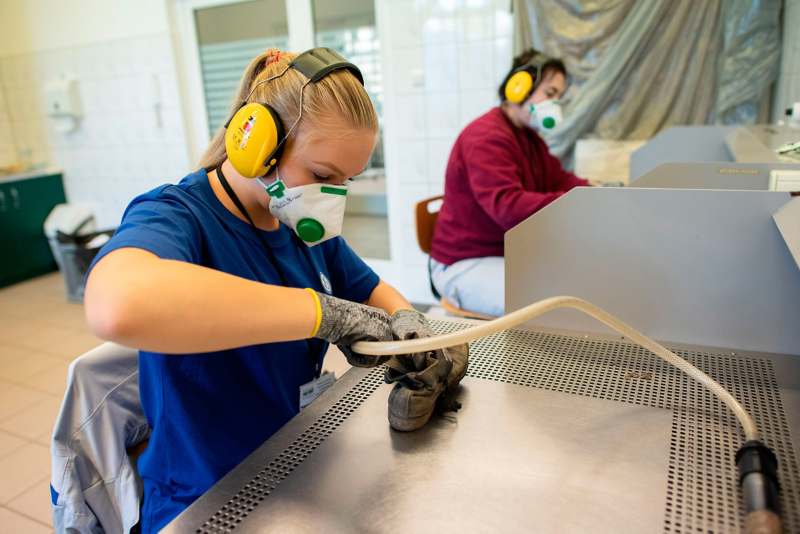 Eine junge VW Mitarbeiterin reinigt in einer Werkstatt Schuhe von KZ-Opfern 