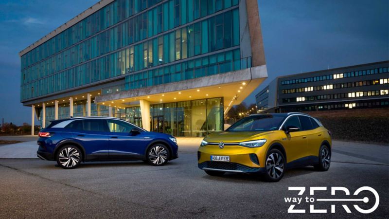 Camionetas eléctricas de Volkswagen en color azul y amarillo, estacionadas frente a edificio moderno.