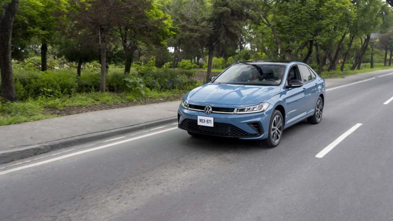 Auto de color azul circula en una avenida cercana a un parque. Jetta 2025 de Volkswagen. 