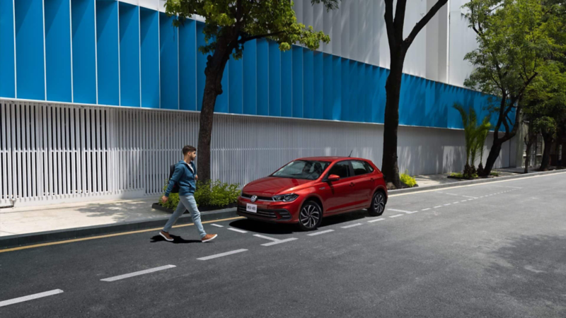 Volkswagen Polo de color rojo circula sobre una calle dentro de la ciudad. 