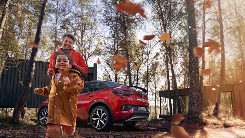 Vista di un padre e una figlia giocare in un parco e dietro di loro parcheggiato un veicolo Volkswagen.