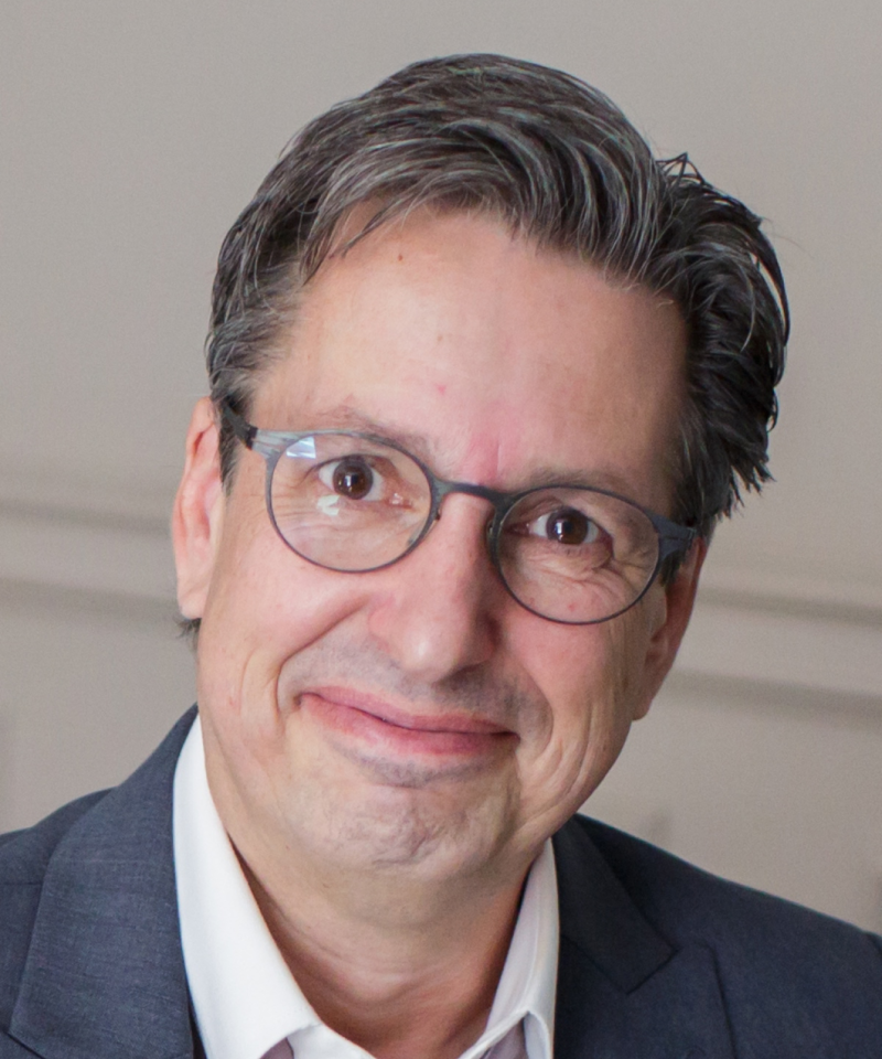 Primo piano di Thomas Bollinger con occhiali e lieve sorriso, sfondo neutro.