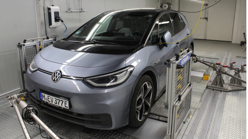 Volkswagen ID.3 grigia in un laboratorio di test, con strumenti di misurazione e una wallbox a parete sullo sfondo.