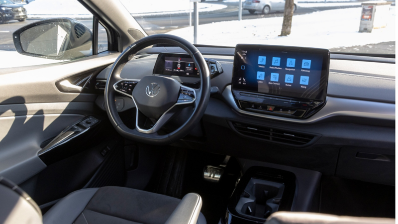 Vista del posto guida di una Volkswagen elettrica con volante e schermo touch centrale con icone di menu visibili.
