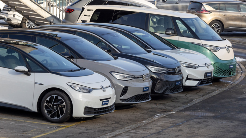 Diversi modelli elettrici Volkswagen parcheggiati affiancati, con un VW ID. Buzz sullo sfondo.
