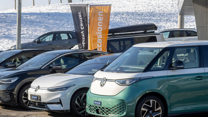 Scheda informativa arancione AMAG Occasions dietro il parabrezza con dati del veicolo, icone e QR code.