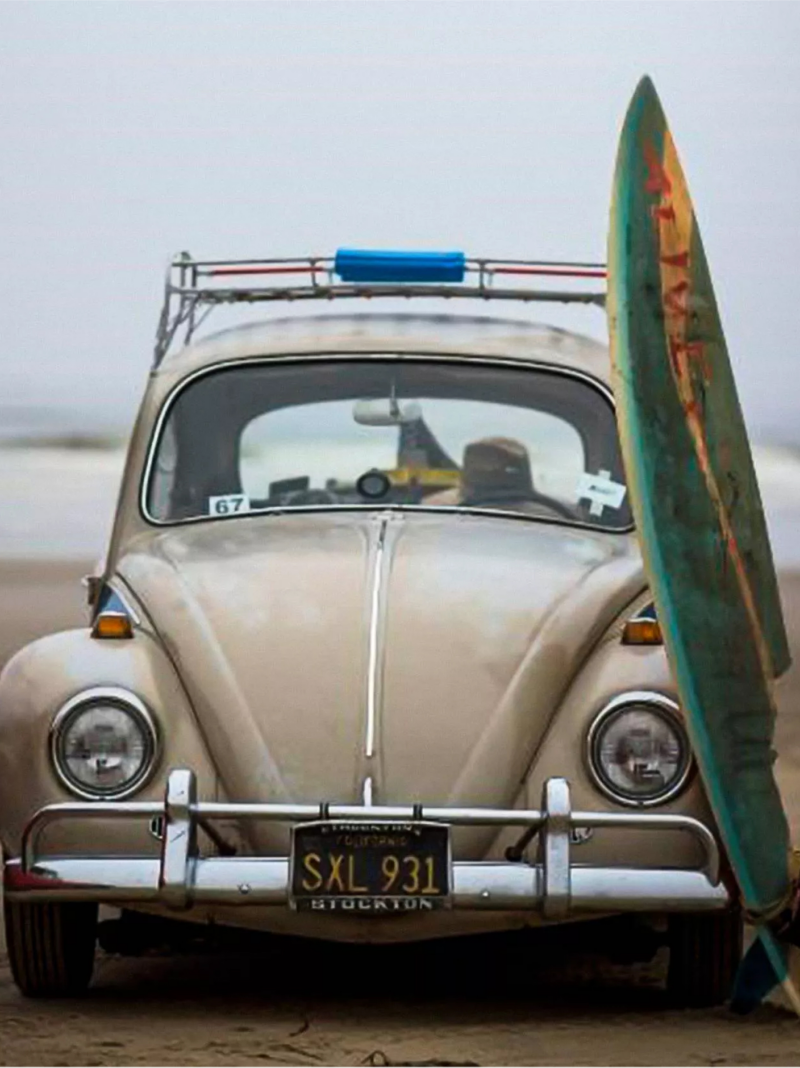 Classic VW beetle with sufboard near beach.