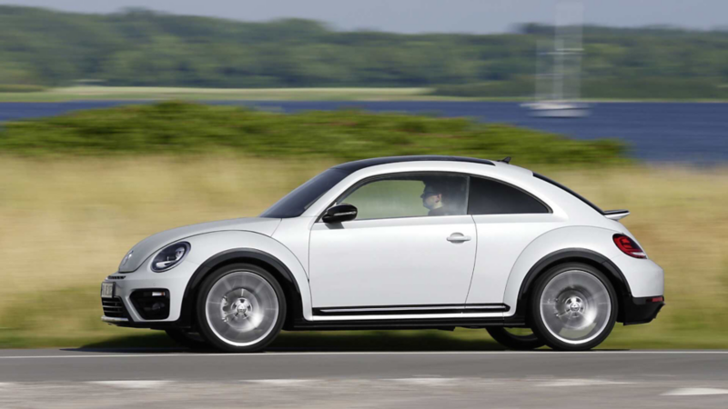 Volkswagen Beetle en color blanco circula dentro de un paisaje boscoso. 