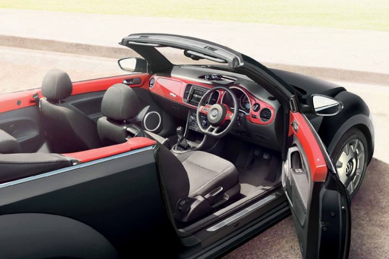 Interior shot of a red Volkswagen Beetle Cabriolet, next to the beach with the roof down and the drivers door open.