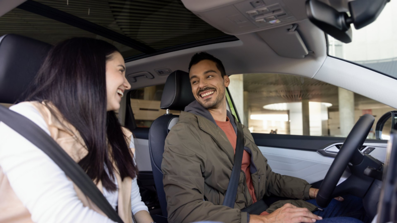 Pareja sonriente disfruta de un viaje en el interior de un Volkswagen con techo panorámico.