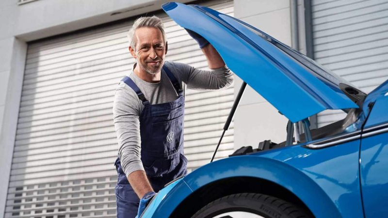 Técnico de Volkswagen abre tapa de cofre de un vehículo de color azul.