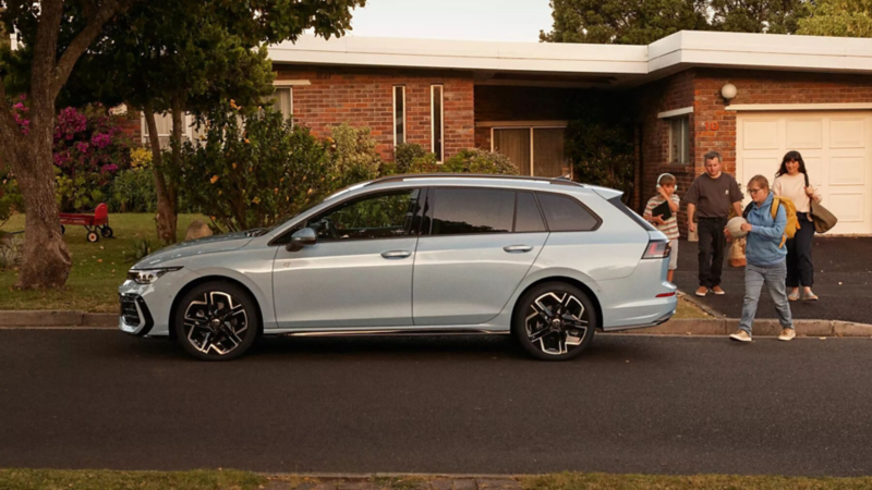 Zijaanzicht van een Golf Variant voor een woning. Een gezin loopt vanuit de woning richting de auto
