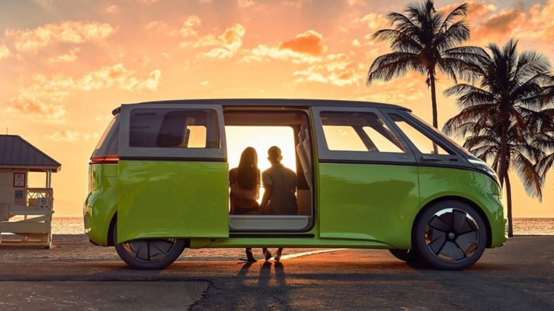 Pareja sentada dentro de Combi eléctrica de Volkswagen estacionada en la playa