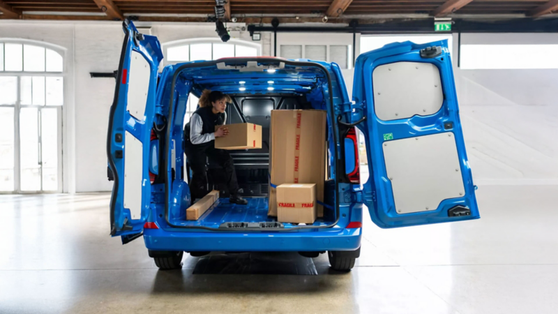 A tradeswoman is loading wooden posts onto the load platform of the VW Transporter panel van.