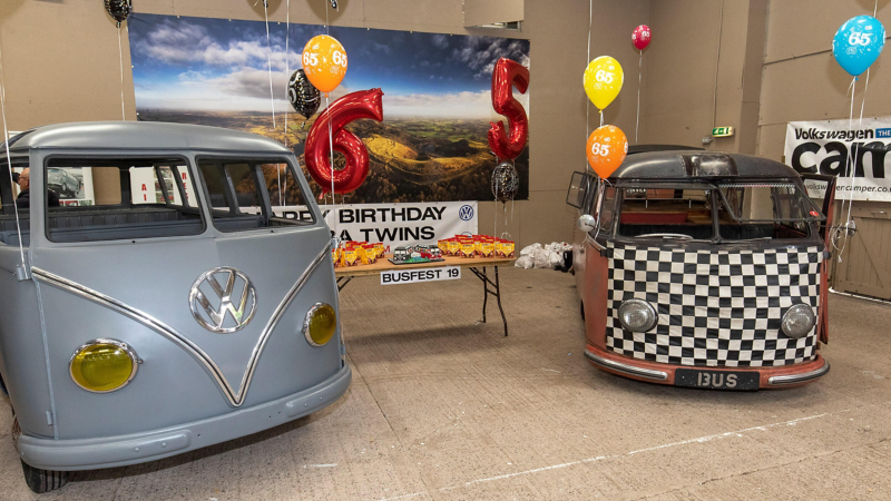 Photo showing 2 VW Samba vans next to balloons and a table with party food on it. 