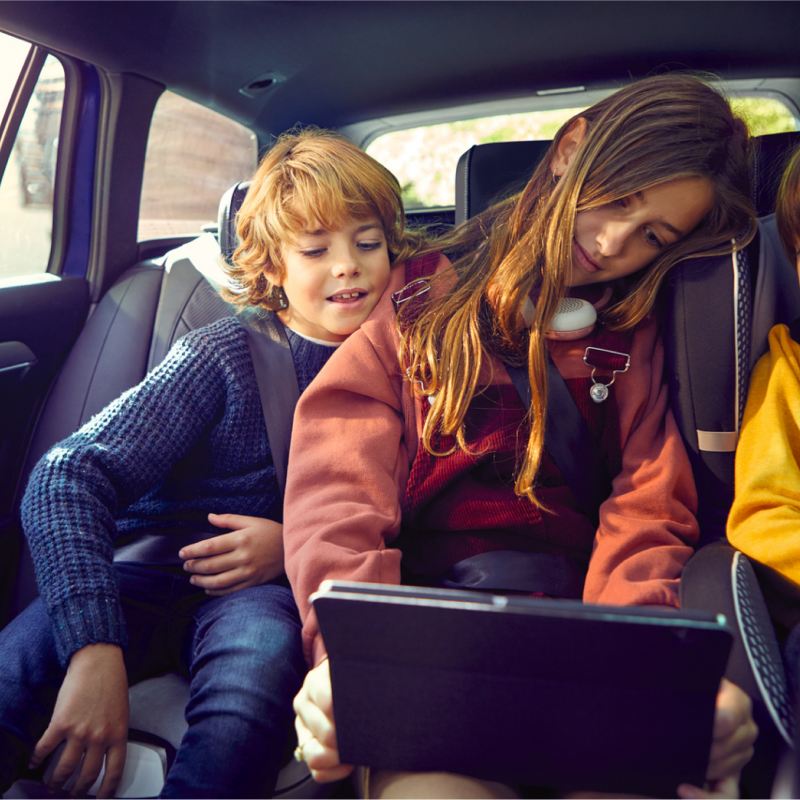 Children using wi-fi connected devices in the back seat of a VW vehicle.
