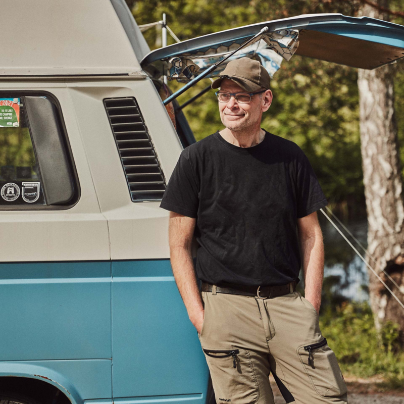 man står vid sin blåa VW folkasbuss campingbil