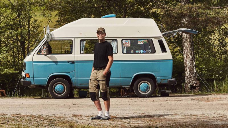 man står vid sin blåa VW folkasbuss campingbil