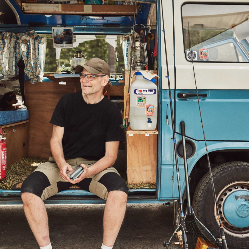 man sitter vid sin blåa VW folkasbuss campingbil
