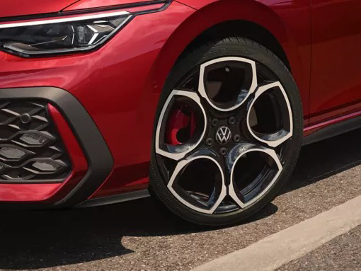 Close-up of the front wheel of a red Volkswagen Golf GTI, showcasing its black and silver five-spoke alloy rim with a red brake caliper.